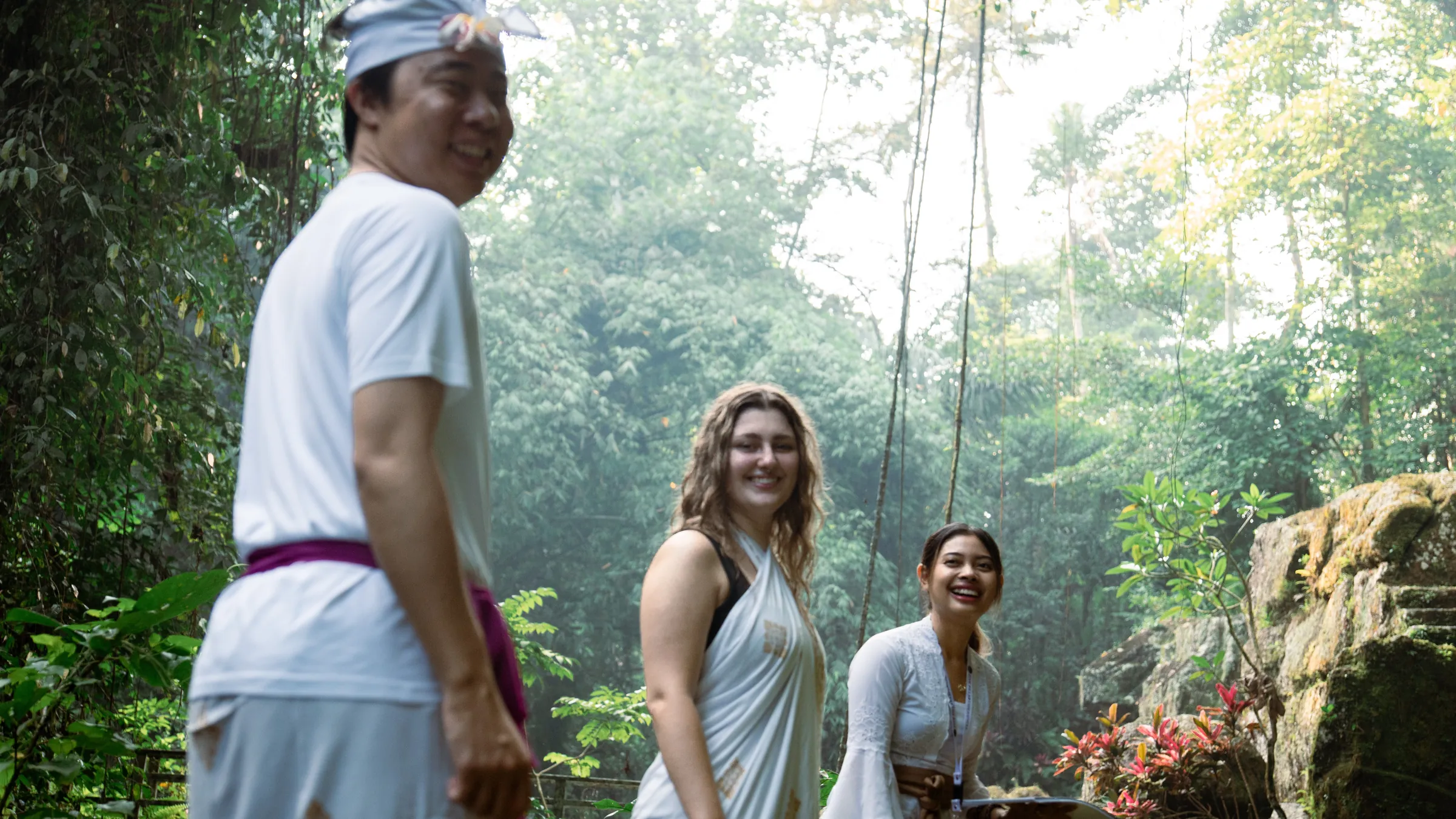 Travelers laughing with a local priest on a misty forest trail before a water blessing
