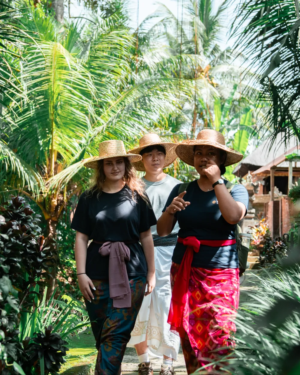 Travelers in woven hats walking through a palm grove with their Balinese host