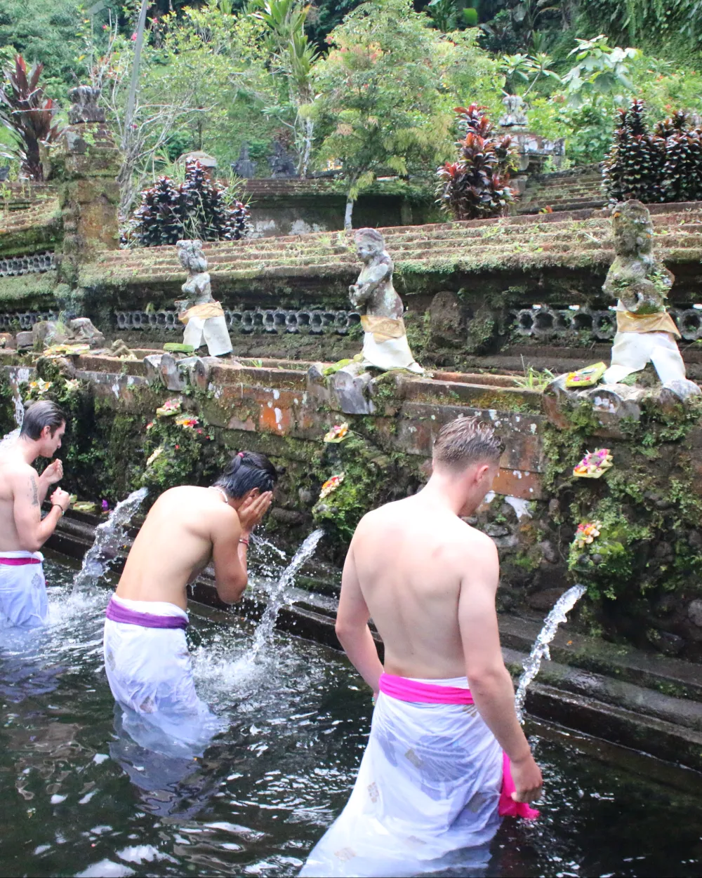 Travelers taking a water blessing under the spouts of a Balinese temple spring